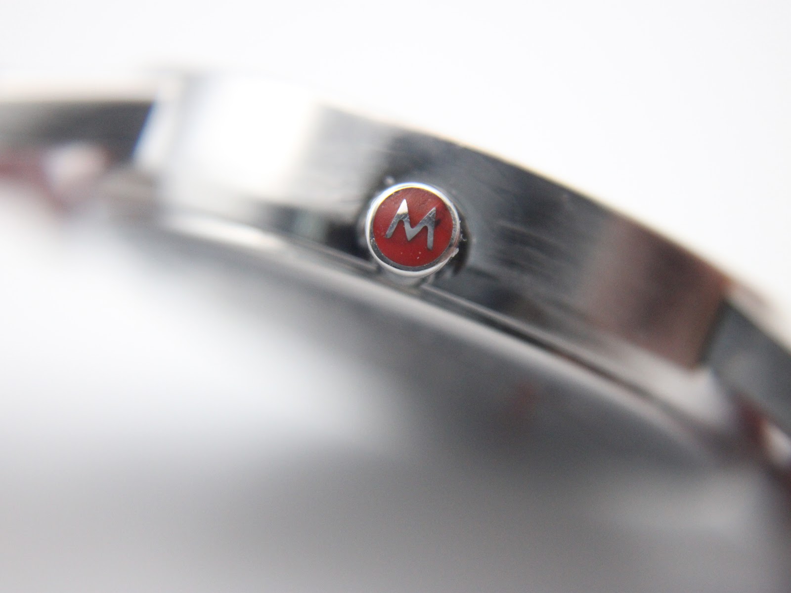 Close-up of the watch crown showing the red M-logo detail.