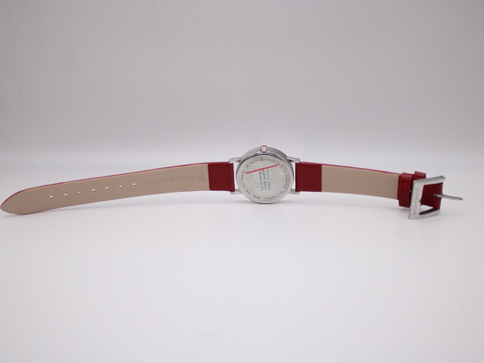 Full length view of the Mondaine watch with the red leather strap laid flat, showcasing the strap's condition and the case back details.