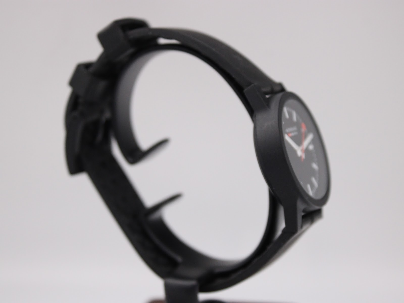 Another side view of the black Mondaine watch on a display stand, highlighting the minimalist design