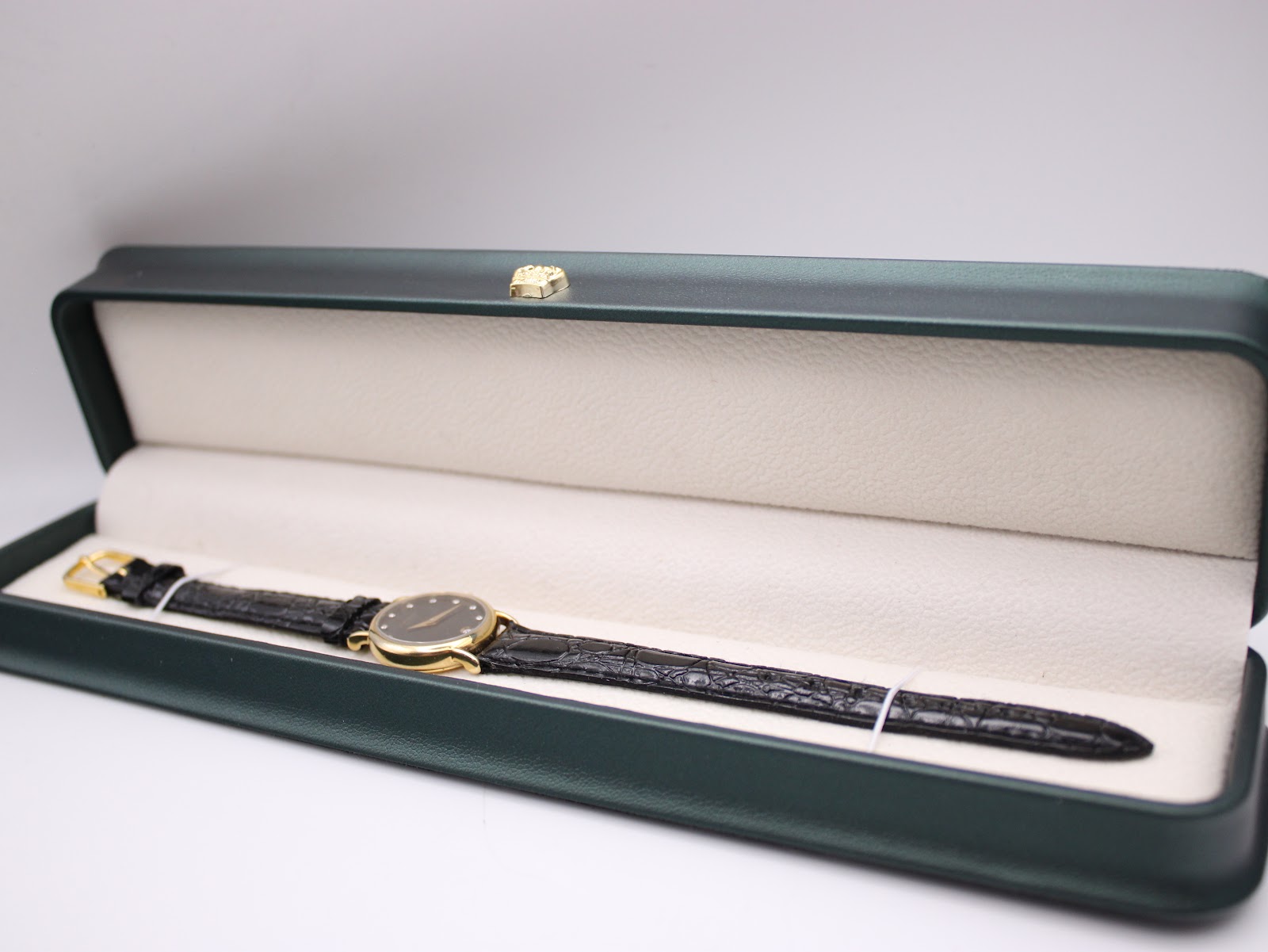 The Raymond Weil watch resting inside a dark green presentation box with a cream interior, laid out flat to display its full length.