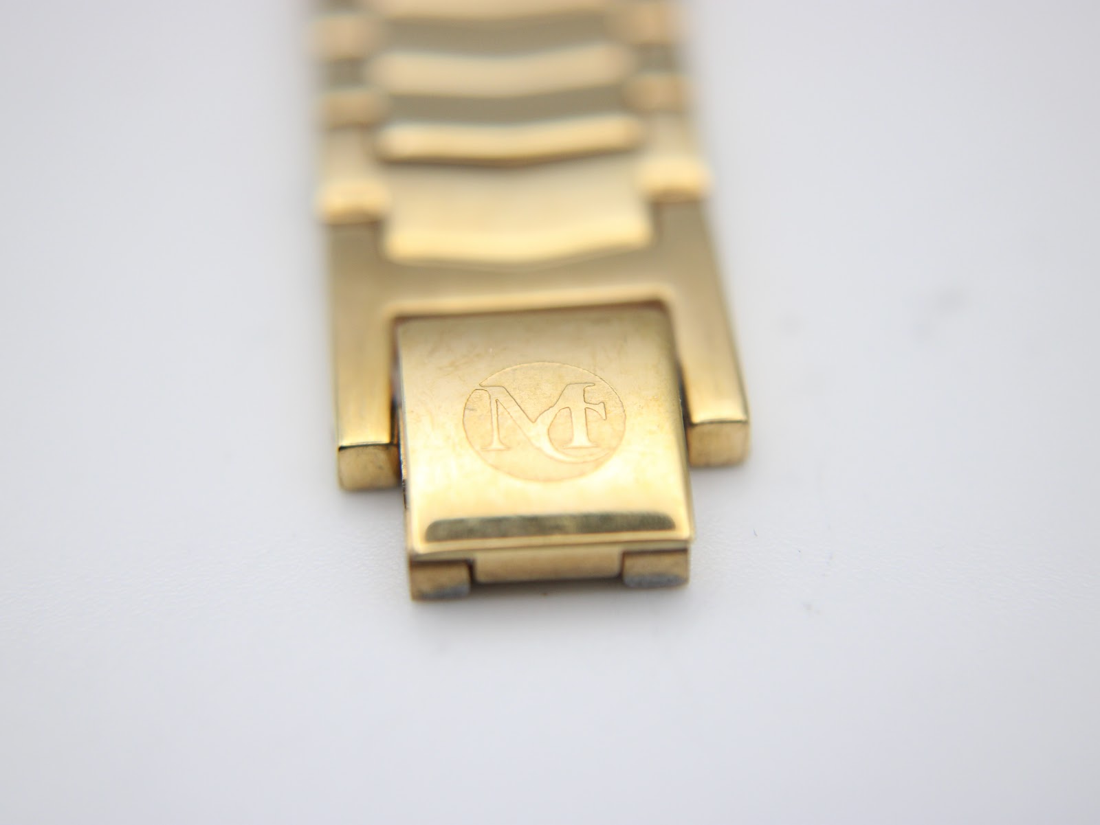 Close-up of the gold-tone folding clasp, displaying the embossed "MC" logo.