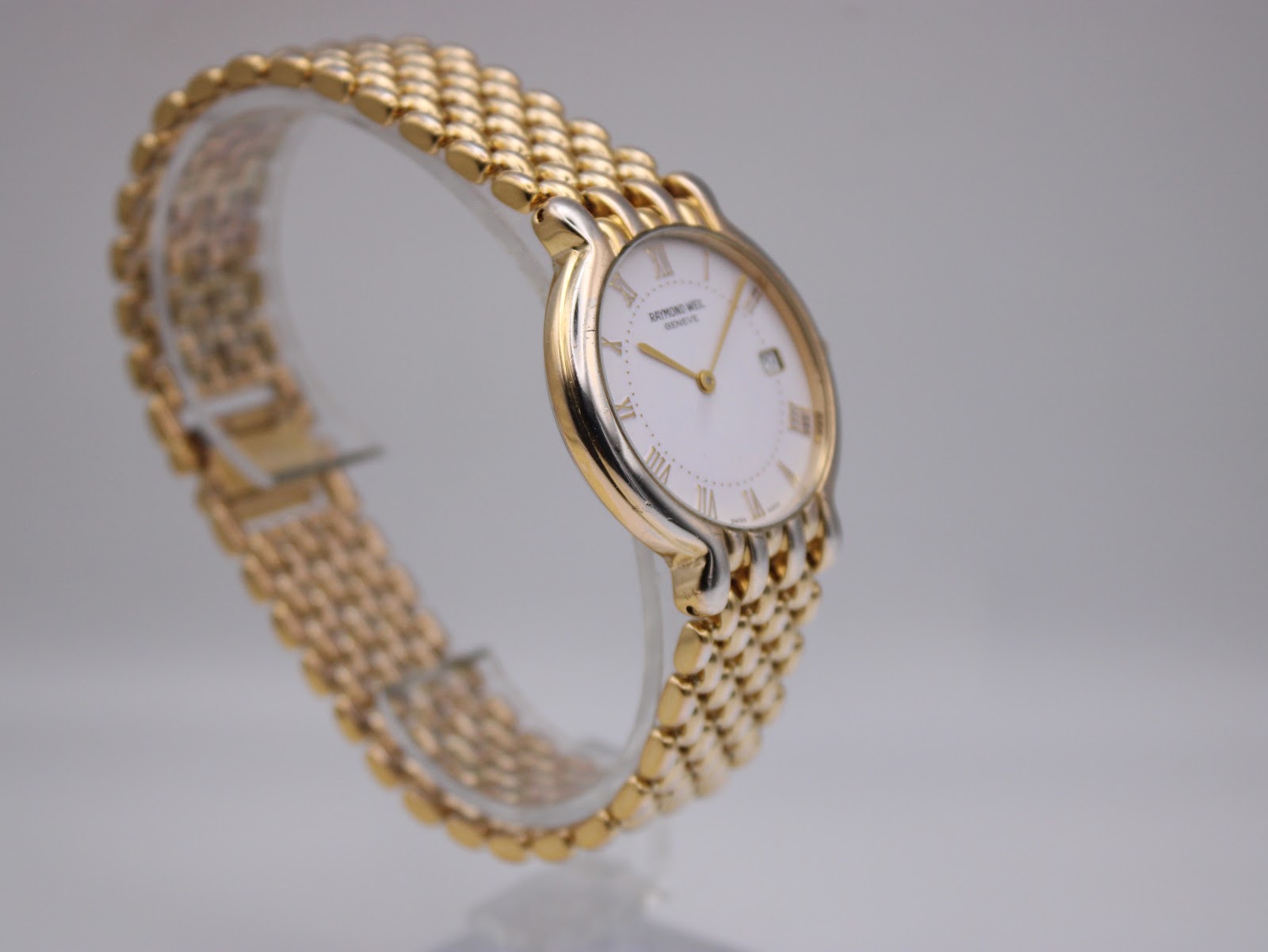 Another angled side view of the Raymond Weil watch, highlighting the case and the textured gold-tone links of the bracelet.