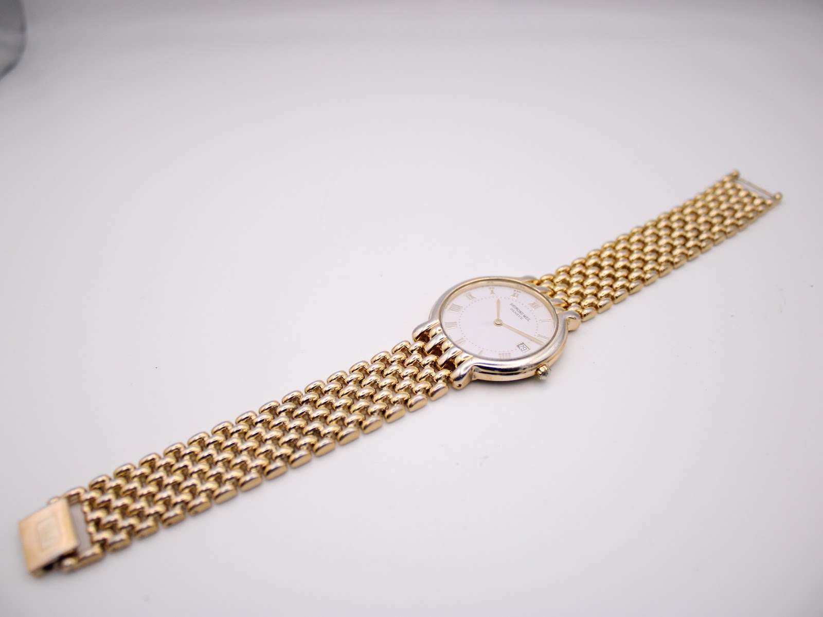 Overhead view of the Raymond Weil watch with its integrated two-tone bracelet extended on a flat surface.