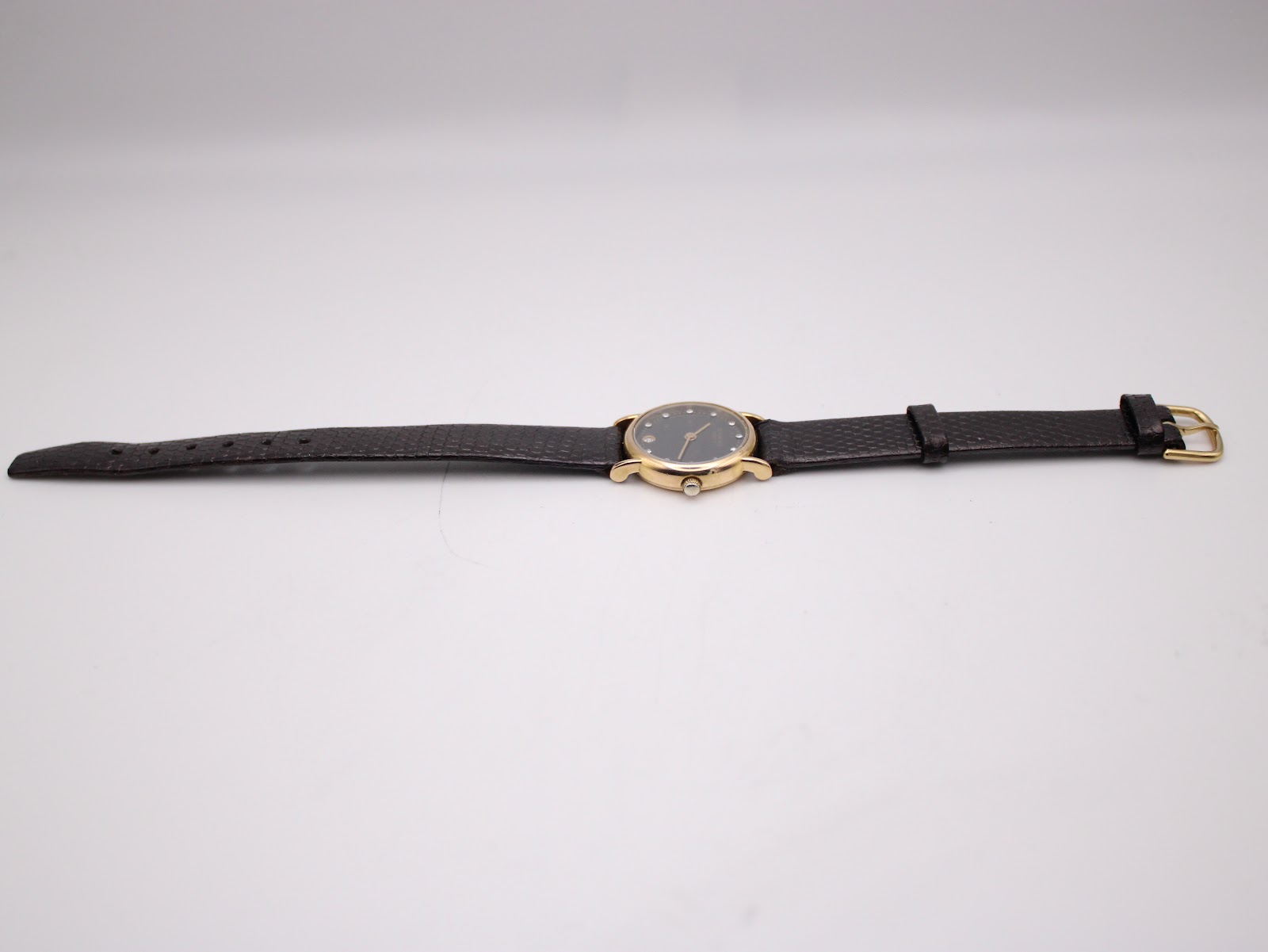 Side view of the Raymond Weil watch with its dark brown leather strap laid flat against a white background, showcasing its full length.