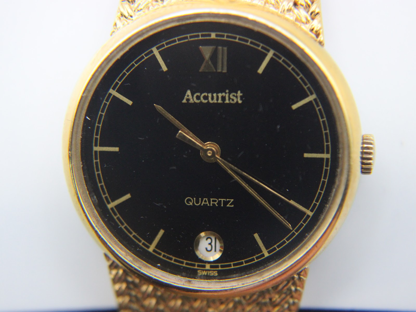 Extreme close-up of the Accurist watch dial, showing 'Accurist', 'QUARTZ', Roman numeral XII, and date window.