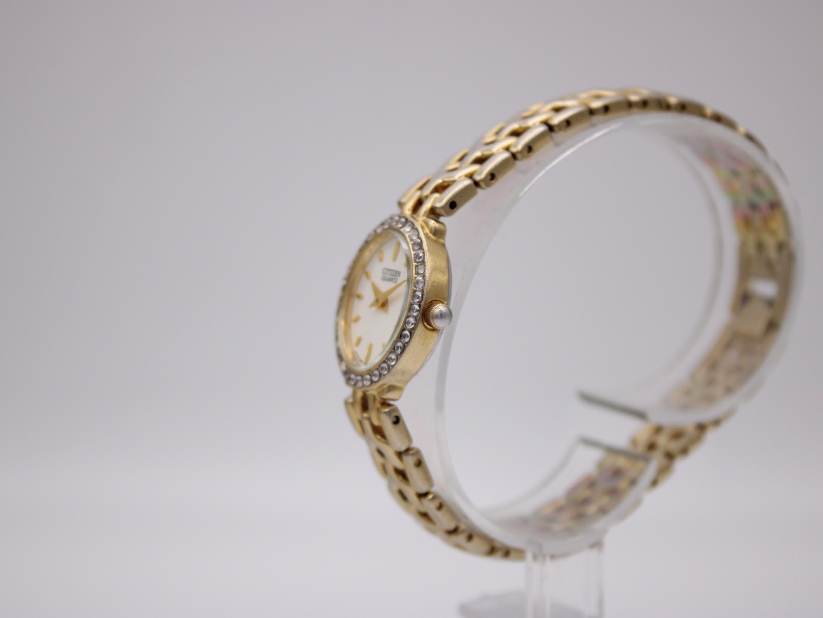 Angled side view of the Citizen watch showing the gold-tone case profile and integrated bracelet on a stand.