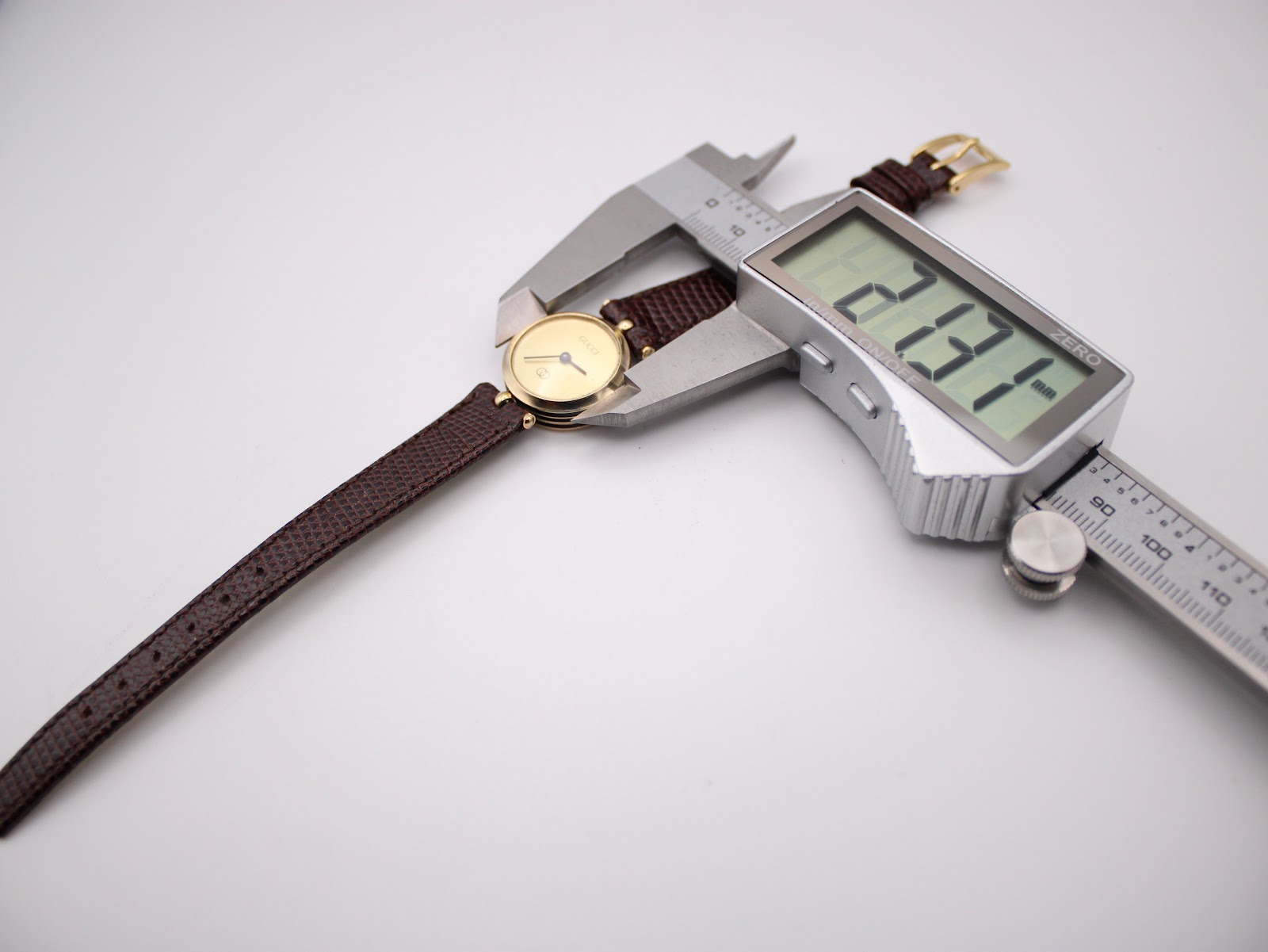 A digital caliper measuring the case diameter of the Gucci watch, displaying a precise measurement of 23.11 mm.