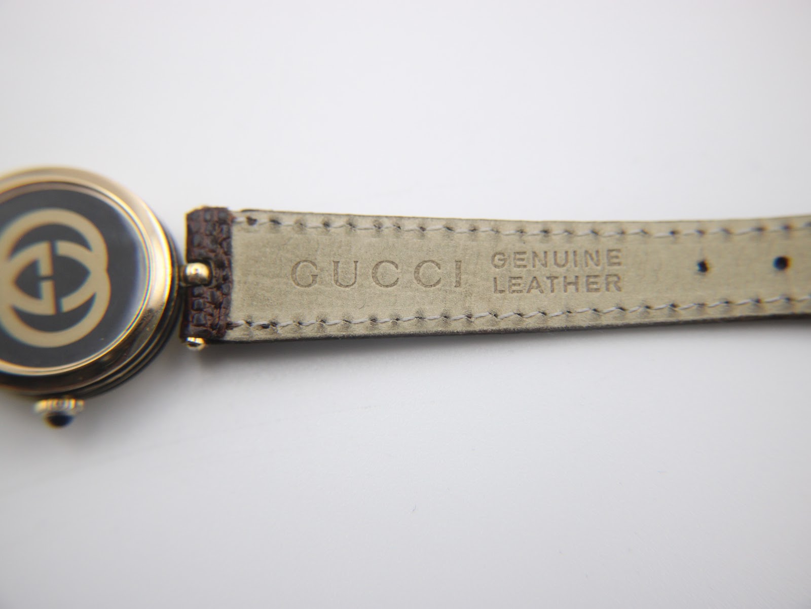 Detailed view of the watch's dark brown leather strap, clearly showing 'GUCCI GENUINE LEATHER' embossed on the underside.