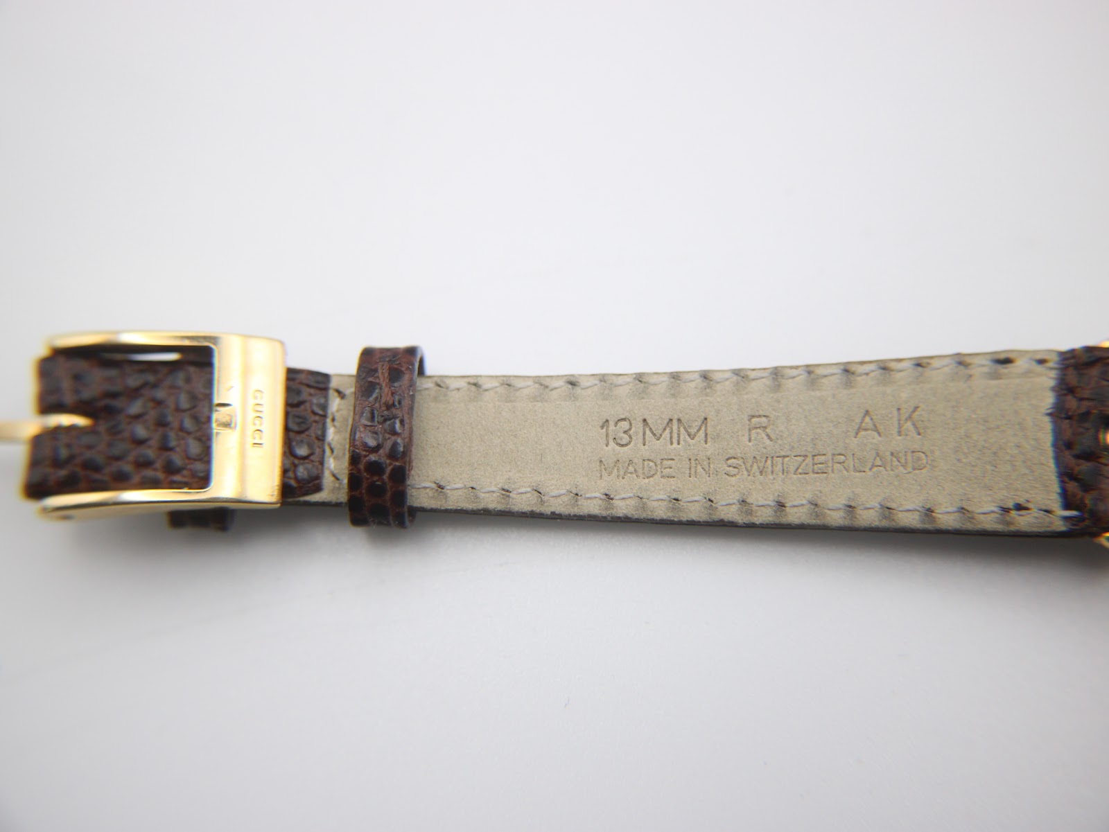 Close-up of the watch strap near the buckle, showing '13 MM R' and 'MADE IN SWITZERLAND' alongside the 'GUCCI' signed gold buckle.