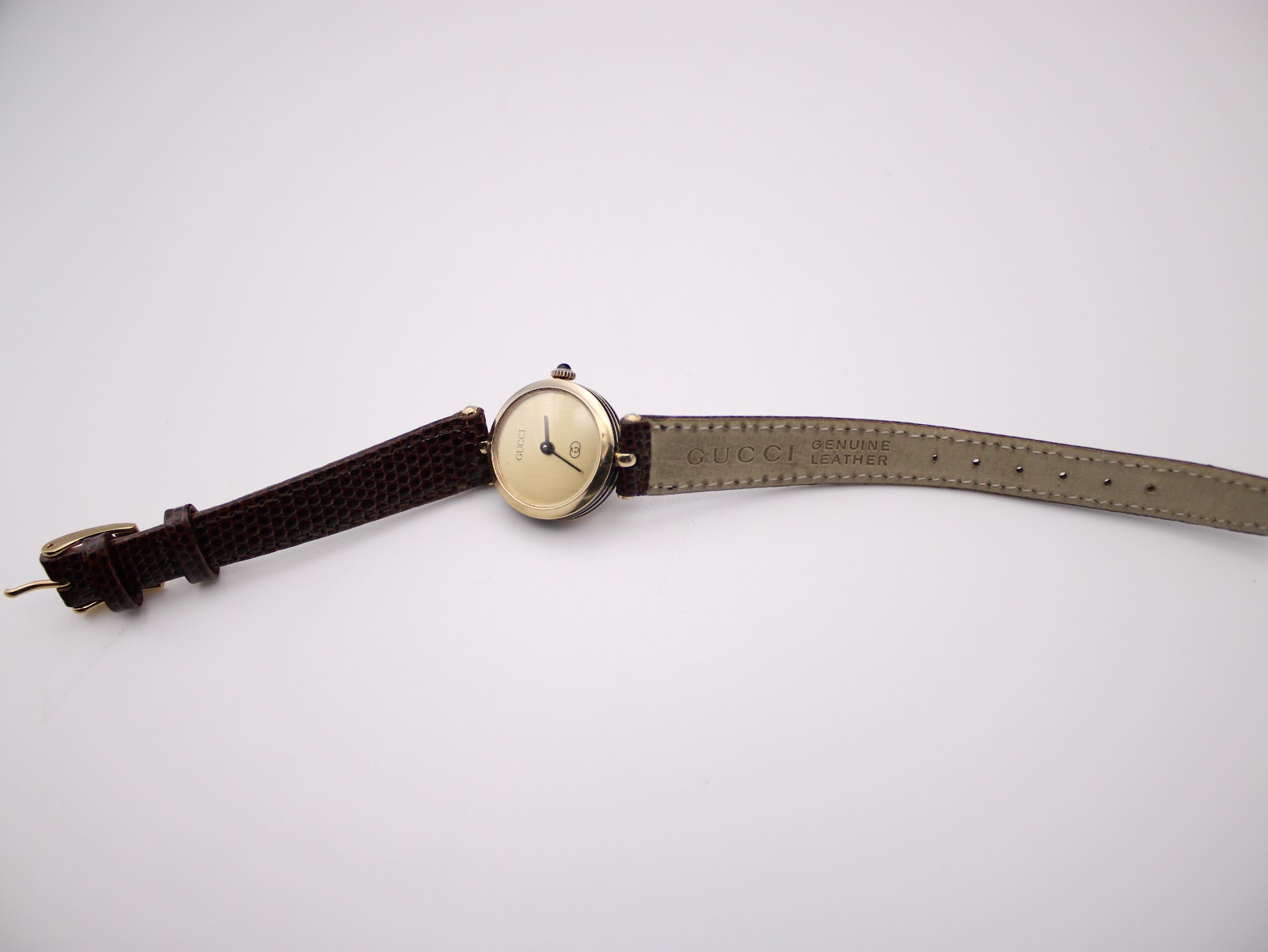 Overhead shot of the Gucci 2000L watch with its dark brown strap fully extended, displaying the gold plated case and dial.