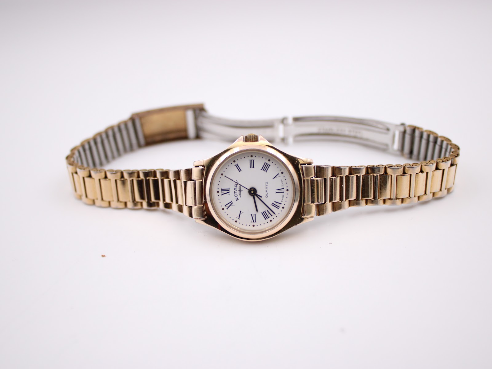 Top-down view of the gold plated Rotary watch with its bracelet unfolded, laid flat on a white background.