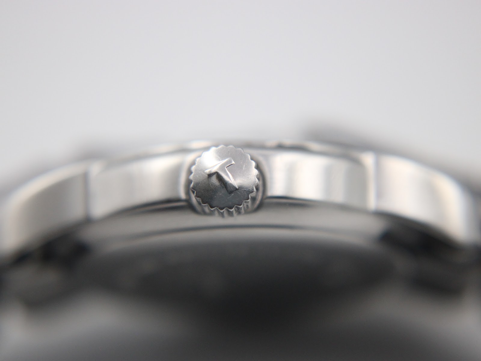 Close-up of the Tissot crown, clearly showing the 'T' logo against the polished case side.