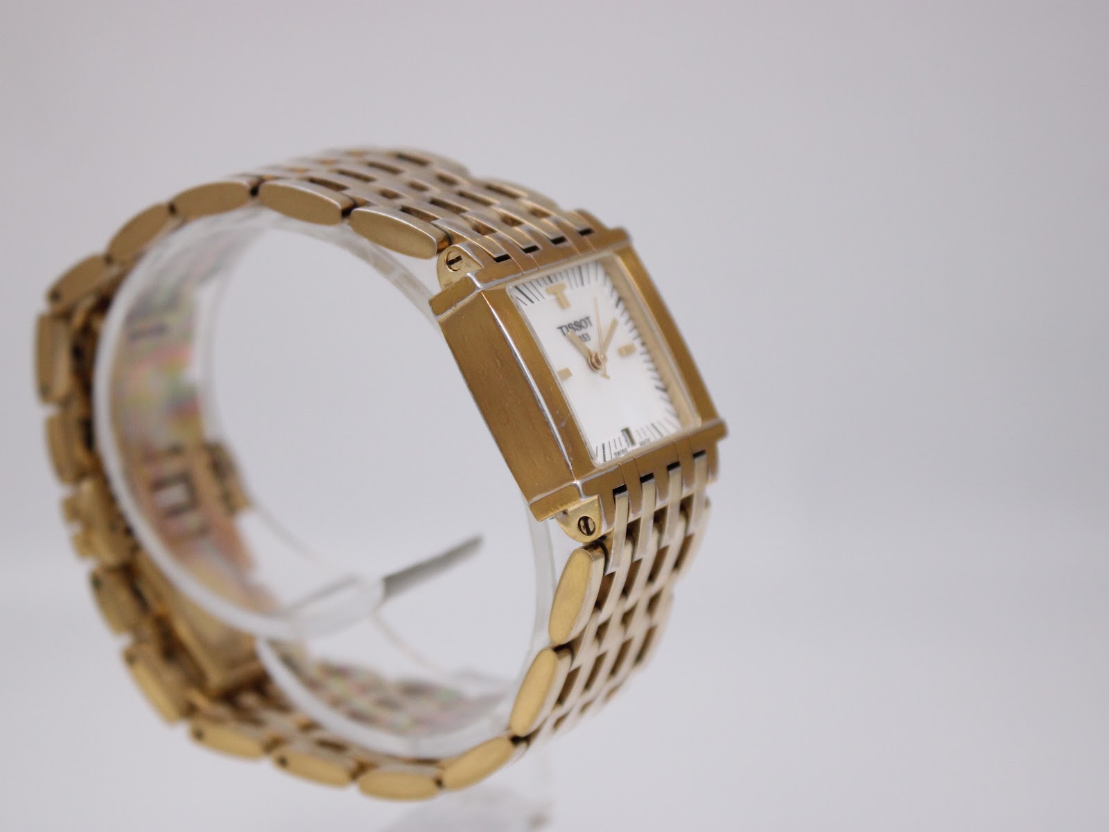 Another side view of the Tissot L910 watch on a clear stand, highlighting the case profile and bracelet links.