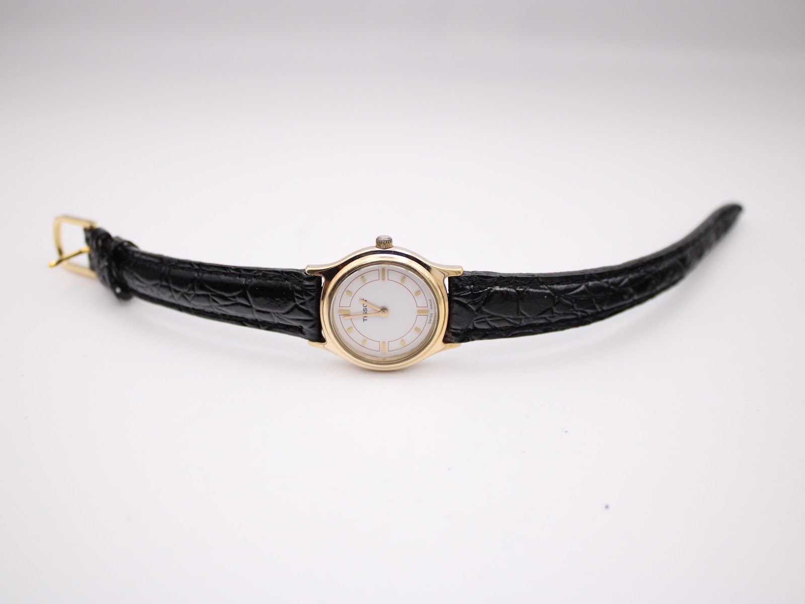 Top-down view of the Tissot watch laid flat, displaying the black leather strap and gold-tone buckle.