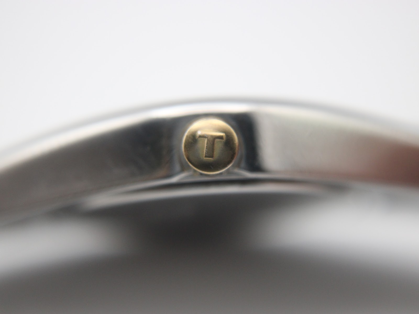 Macro shot of the gold-tone crown, clearly showing the embossed Tissot 'T' logo.