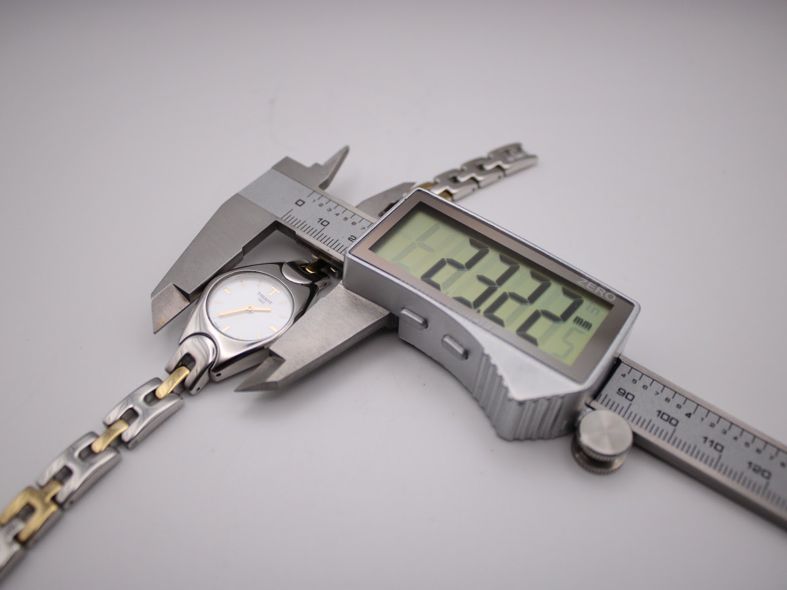 A digital caliper measuring the watch case, displaying a precise measurement of 23.22 mm in width.