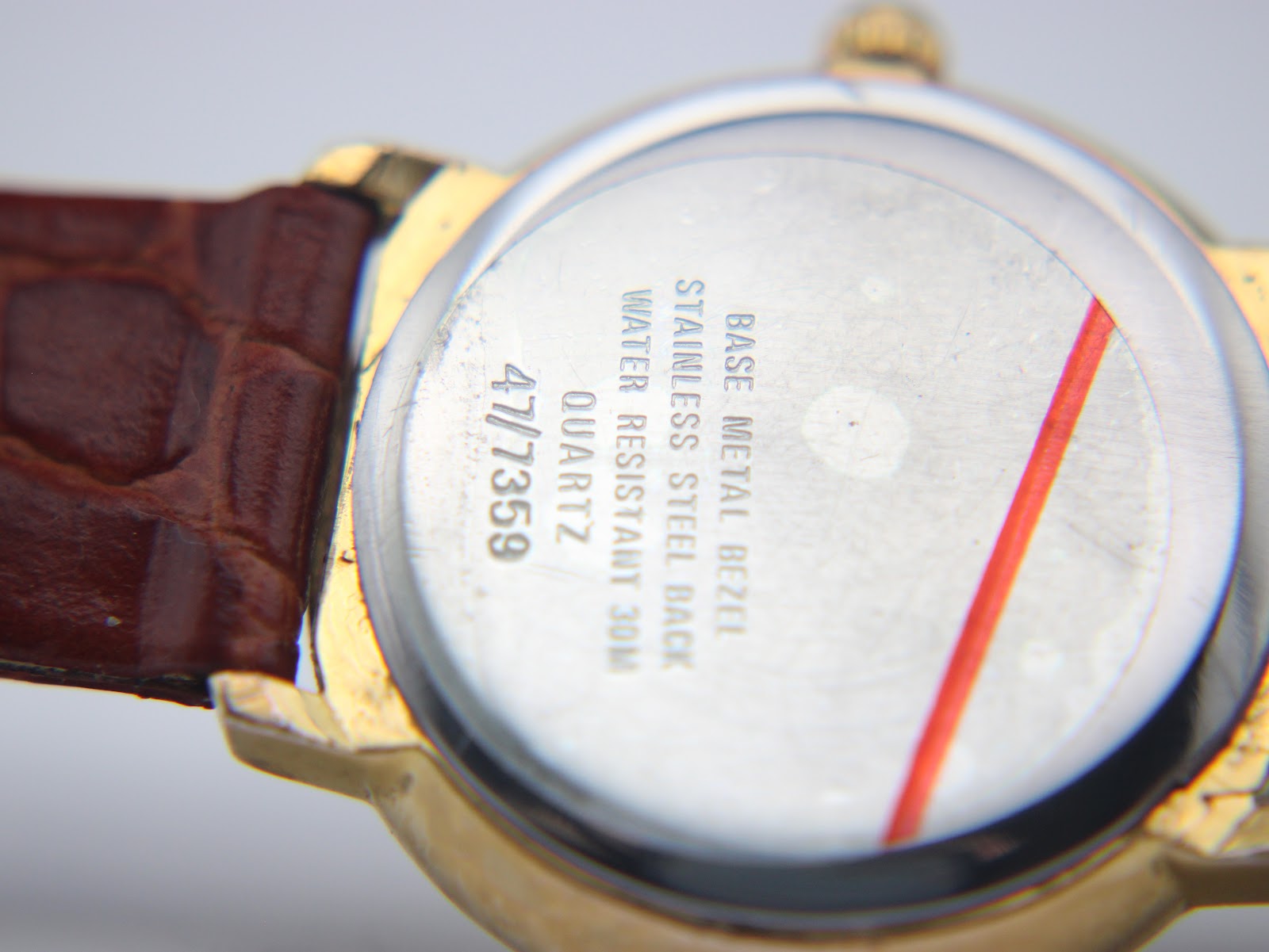 Close-up of the watch case back, showing 'BASE METAL BEZEL STAINLESS STEEL BACK WATER RESISTANT 30M QUARTZ 47/7359' engravings.