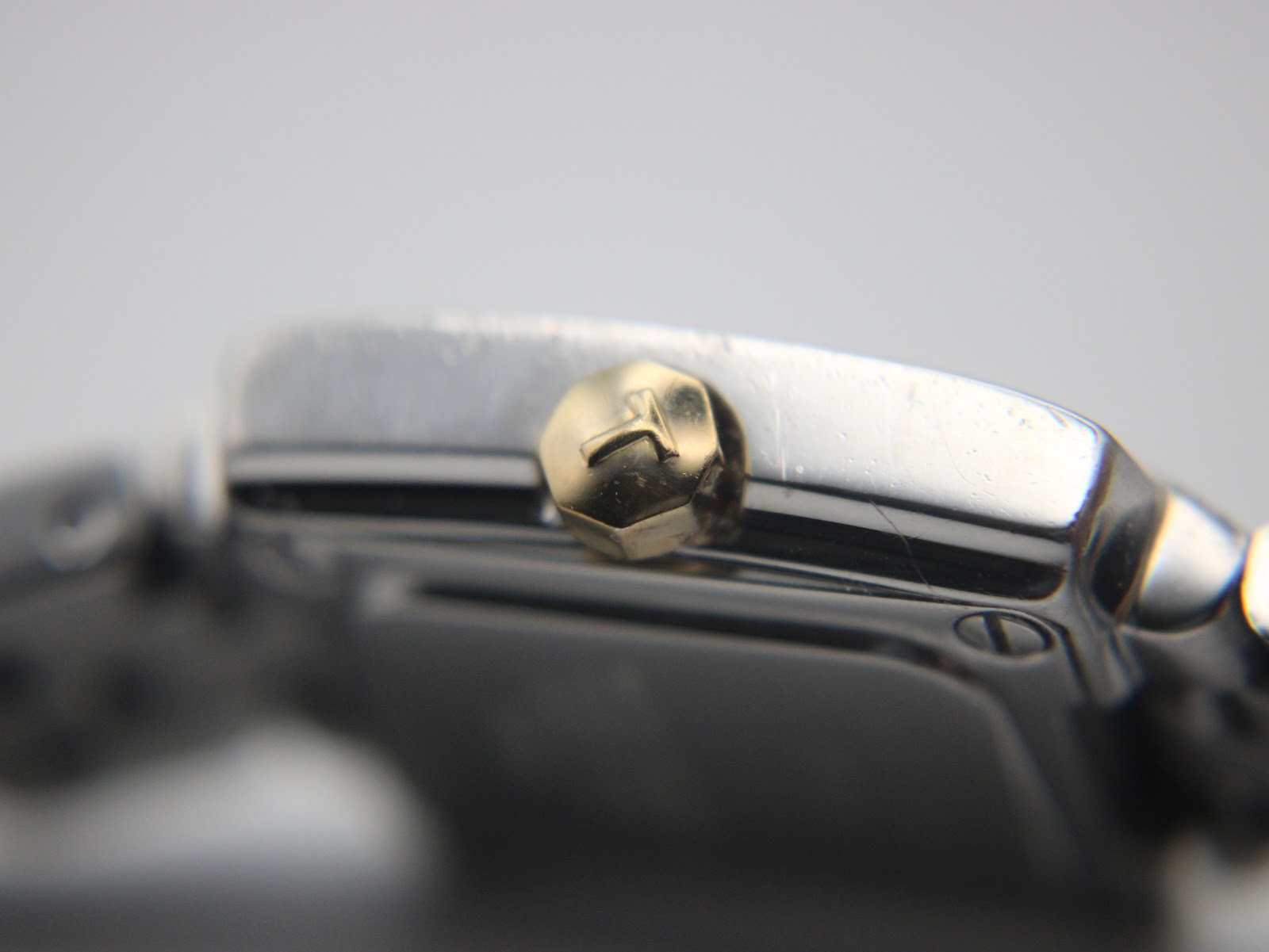Macro close-up of the gold-tone crown of the Tissot T-Trend watch, showing its textured finish and embossed 'T' logo.