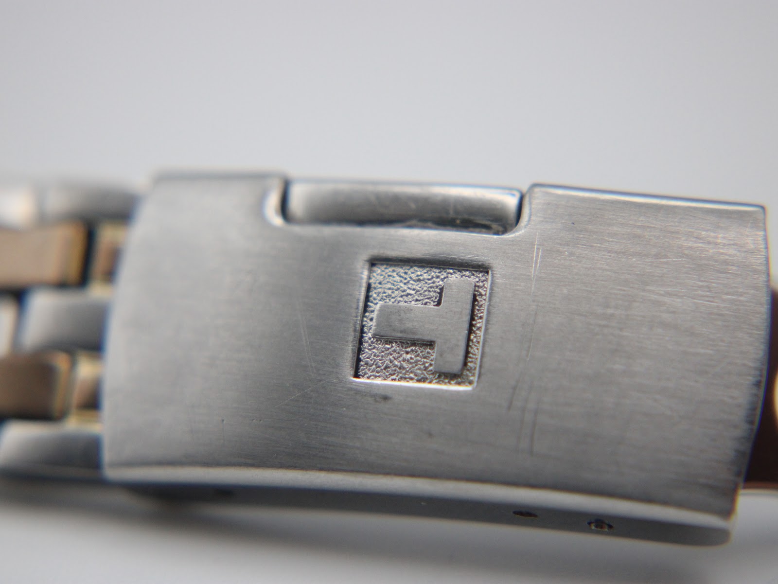 Close-up of the hidden butterfly deployant clasp of the Tissot bracelet, featuring a textured square with the Tissot 'T' logo.