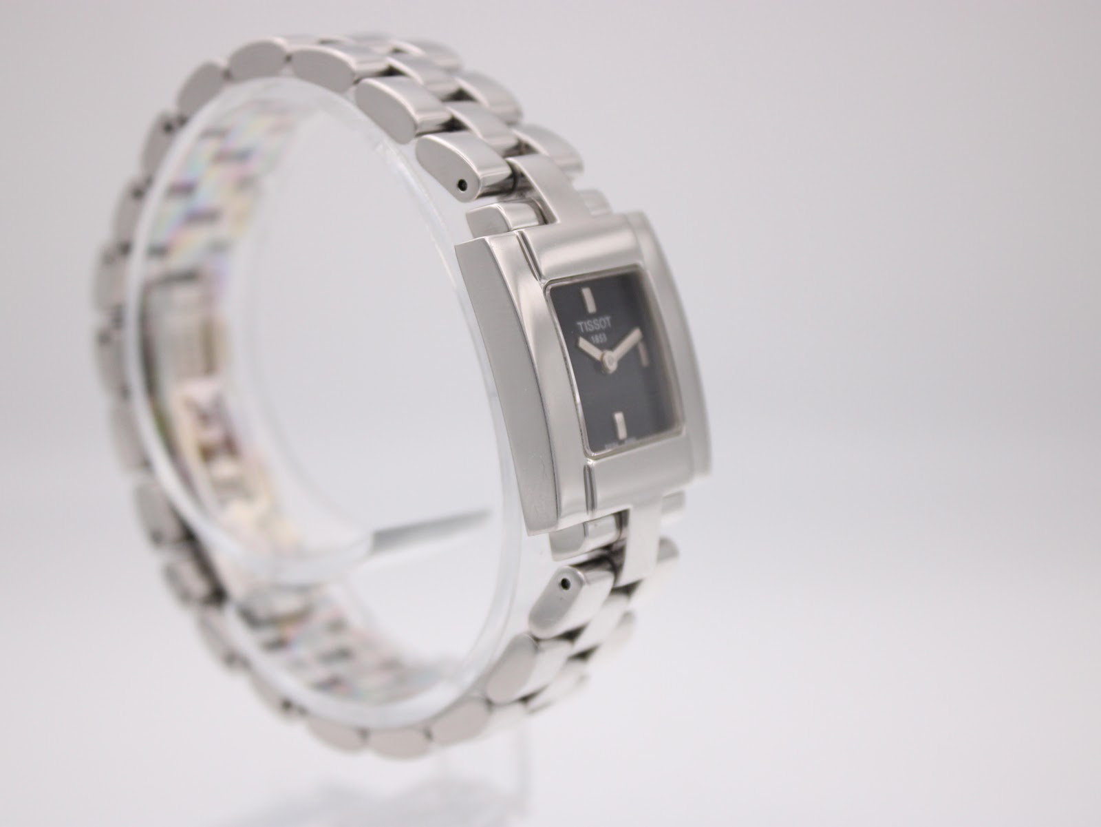 Side view of the Tissot L730K watch on a clear display stand, highlighting the integrated bracelet design.