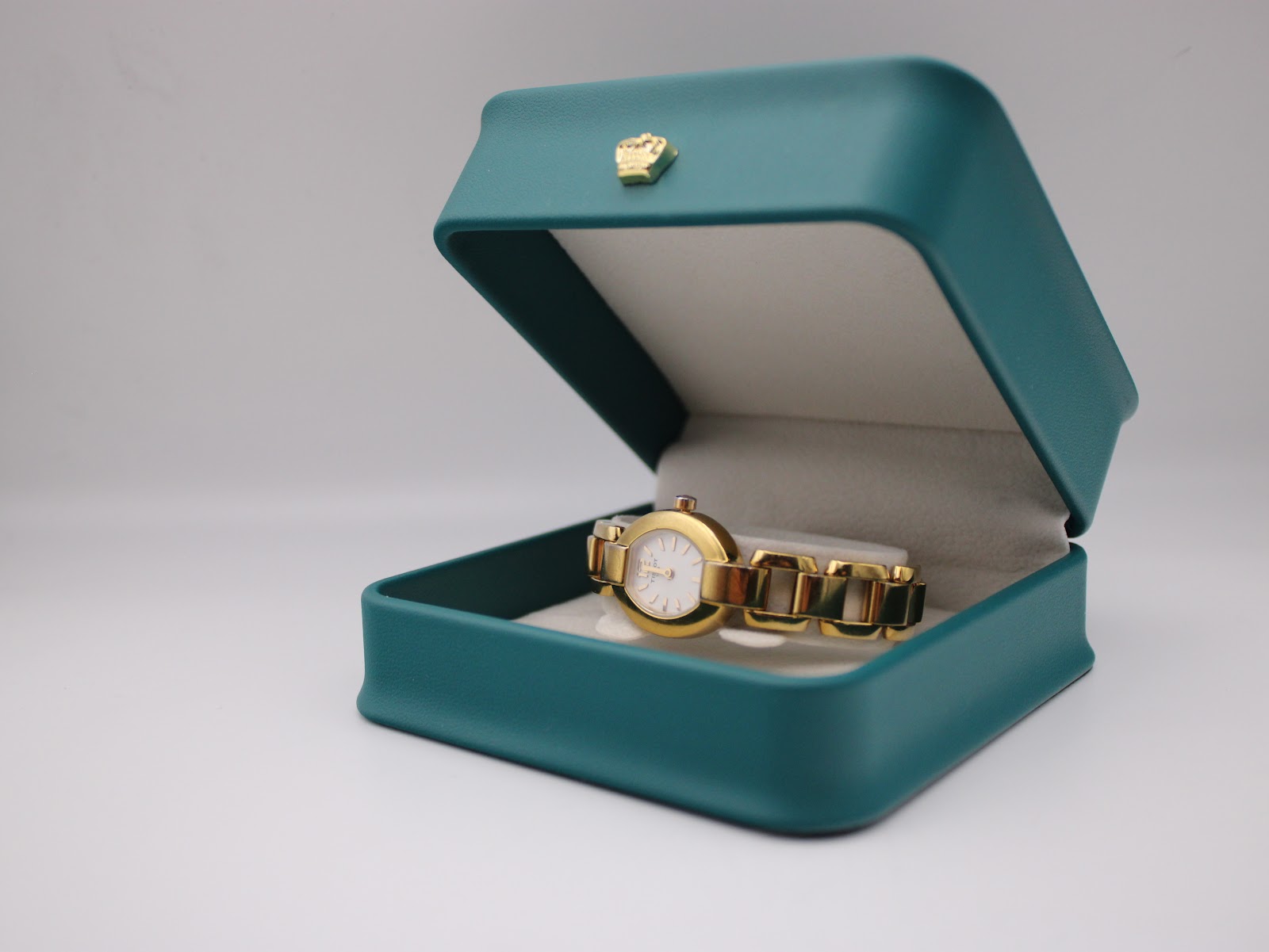 The gold-tone Tissot G332 watch resting inside an open teal presentation box with a cream interior.
