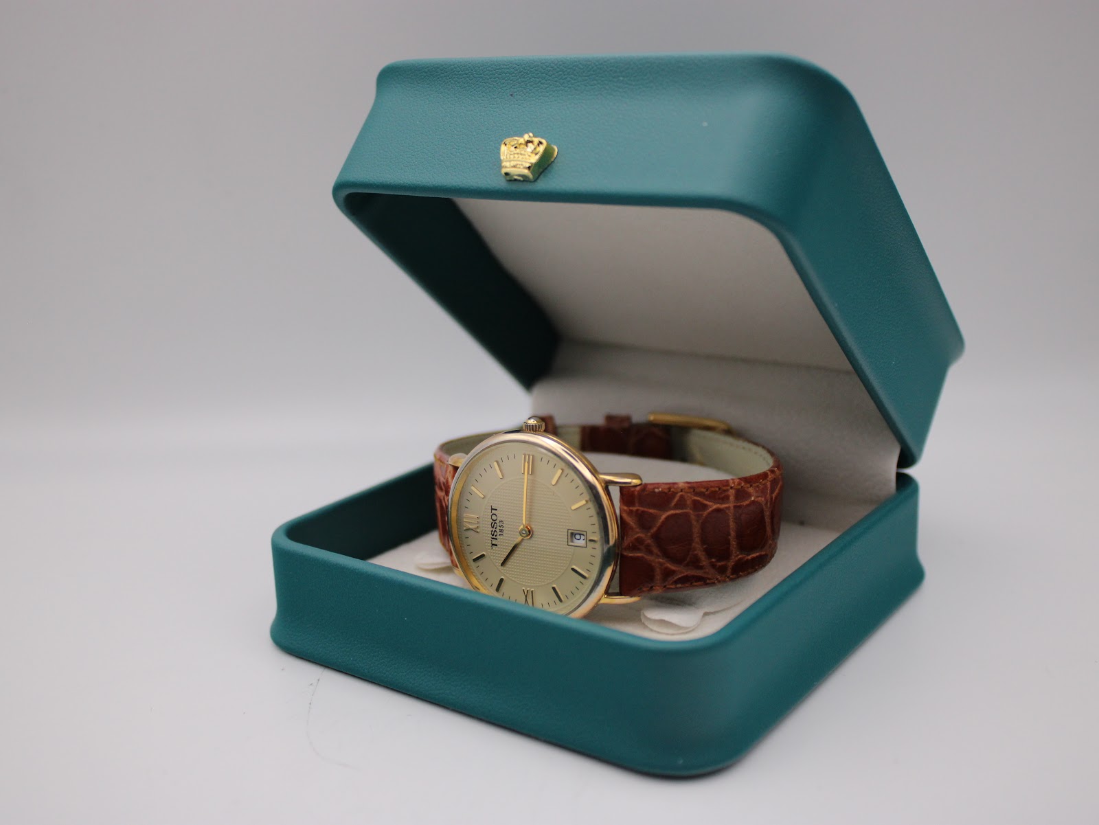 Tissot T890K watch presented open in a teal-coloured watch box with a gold crown emblem on the lid.