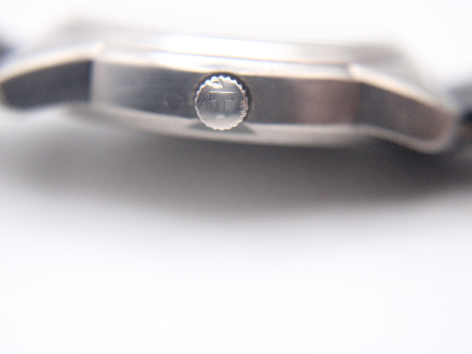 Macro shot of the Tissot 'T' signed crown on the side of the titanium watch case.