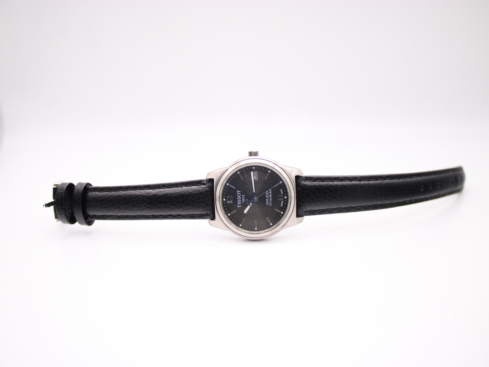 Full length view of the Tissot watch with black leather strap laid flat on a white background.