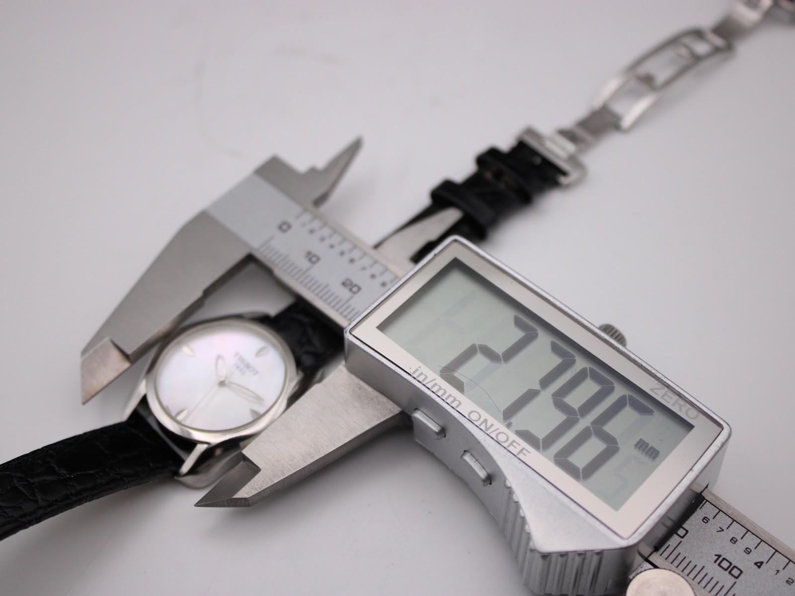 Digital caliper measuring the Tissot watch case diameter, displaying an exact measurement of 27.96mm on a white background.
