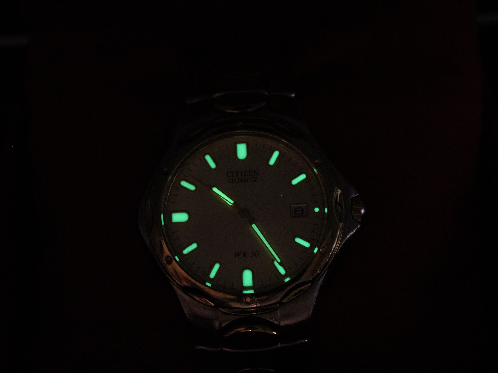 Dark shot of the Citizen watch dial, demonstrating the luminous gold-tone hands and hour markers glowing.