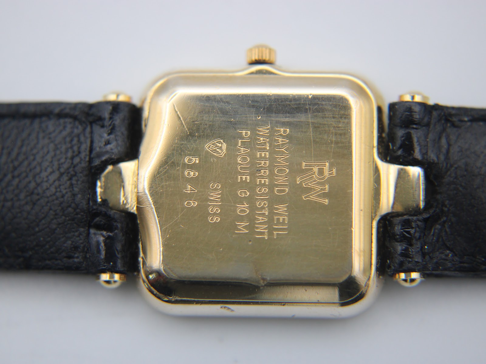 Close-up of the gold-plated case back, showing 'RAYMOND WEIL', 'RW' logo, 'WATERRESISTANT', 'PLAQUE G 10 M', 'SWISS', and model number '5846', with wear marks visible.