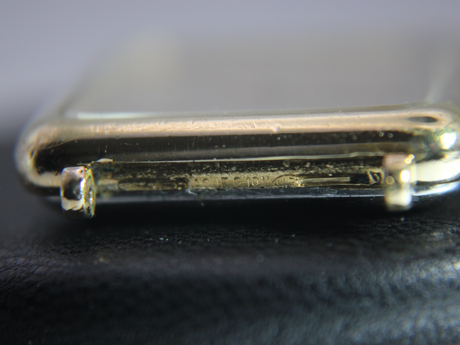 Extreme close-up of the side of the gold plated case, showing the "PLAQUE G 10 M" stamp indicating 10 micron gold plating.